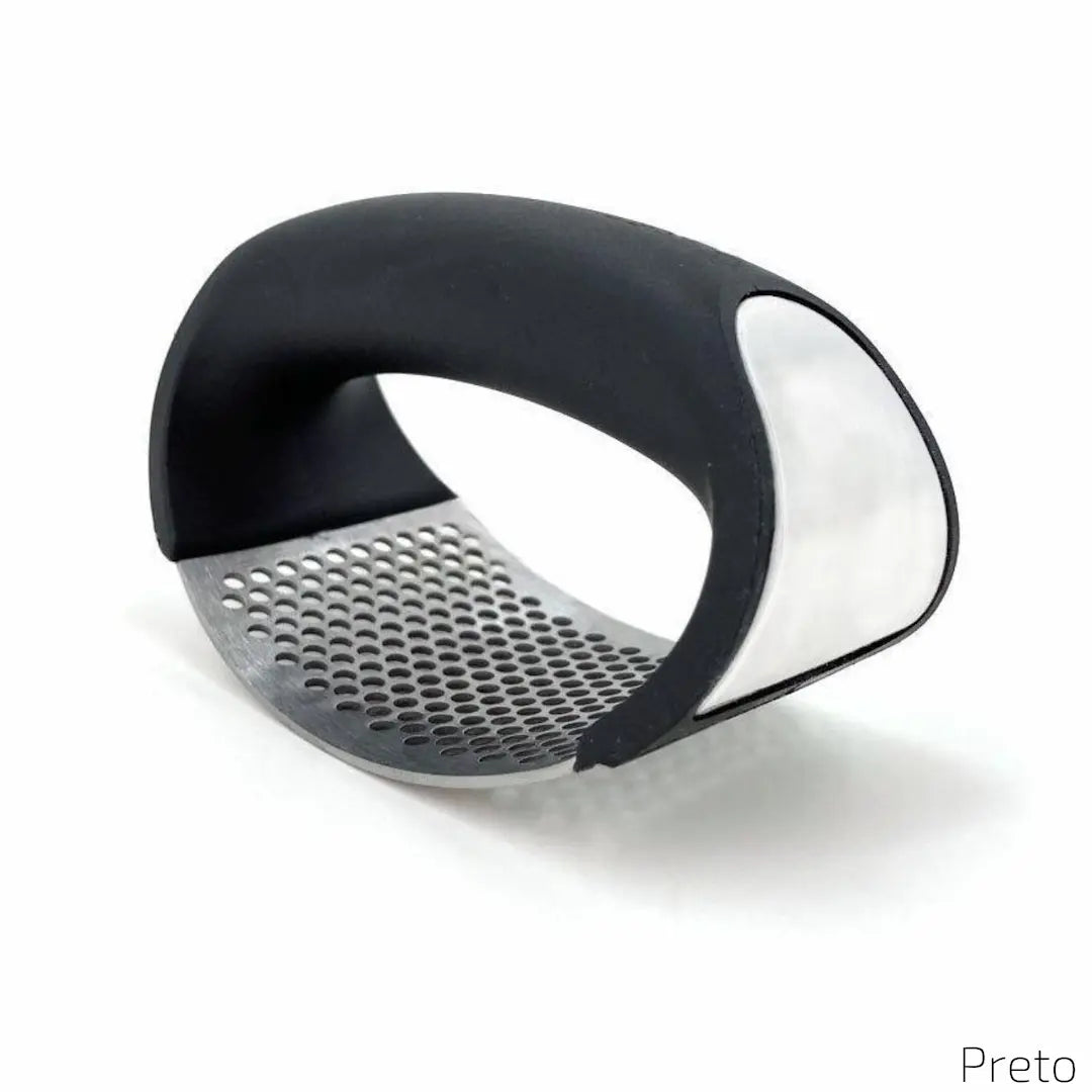 A imagem mostra um amassador de alho com cabo curvado na cor preta e uma superfície metálica perfurada para triturar alimentos. O design é ergonômico, moderno e funcional, proporcionando facilidade no preparo de temperos. No canto inferior direito, está o texto "Preto".