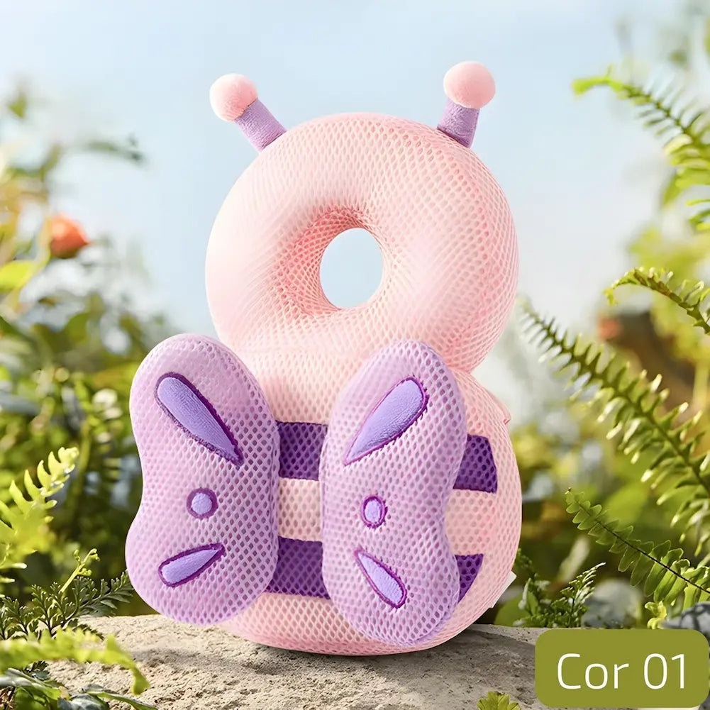  A imagem mostra uma almofada anti-queda para bebês em formato de borboleta. A almofada é de cor rosa clara com detalhes em lilás, incluindo as asas da borboleta. Possui um buraco central para proteger a cabeça do bebê. A almofada está situada em um ambiente natural com plantas verdes ao redor, transmitindo uma sensação de segurança e conforto. No canto inferior direito, há a indicação "Cor 01".