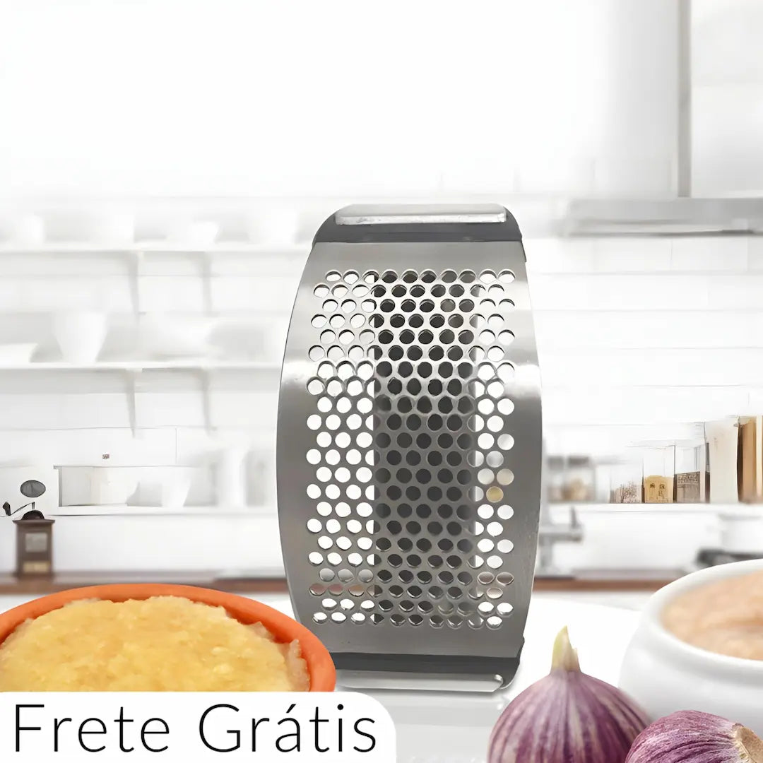 A imagem mostra um ralador de metal, com uma estrutura perfurada que facilita a tarefa de ralar alimentos como alho, queijo ou outros ingredientes. O ralador está posicionado em uma superfície de cozinha, com cebolas e um recipiente com comida ao fundo. A legenda "Frete Grátis" sugere uma promoção ou incentivo de compra para o produto.