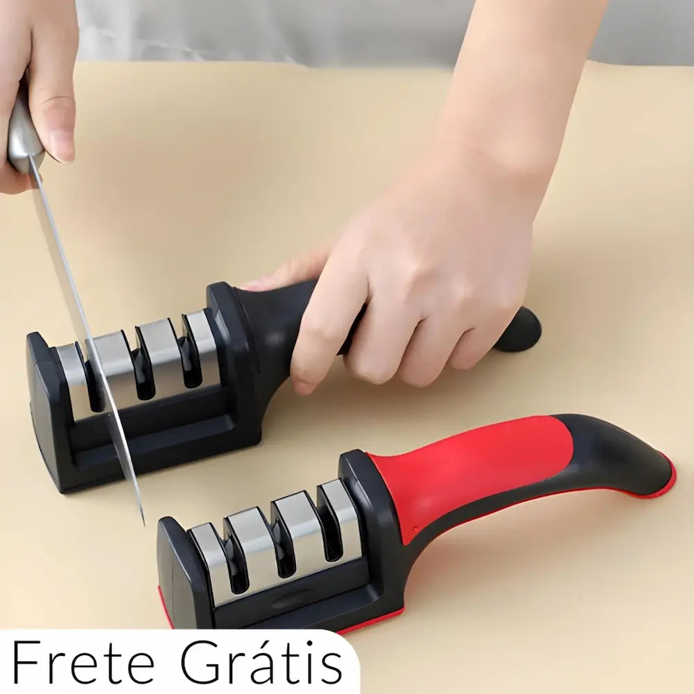  Imagem de duas mãos utilizando um afiador de facas manual. A mão esquerda segura uma faca enquanto a direita segura o afiador, que possui três slots de afiação. Outro afiador semelhante, com detalhes em vermelho, está ao lado. Texto na parte inferior esquerda diz "Frete Grátis".