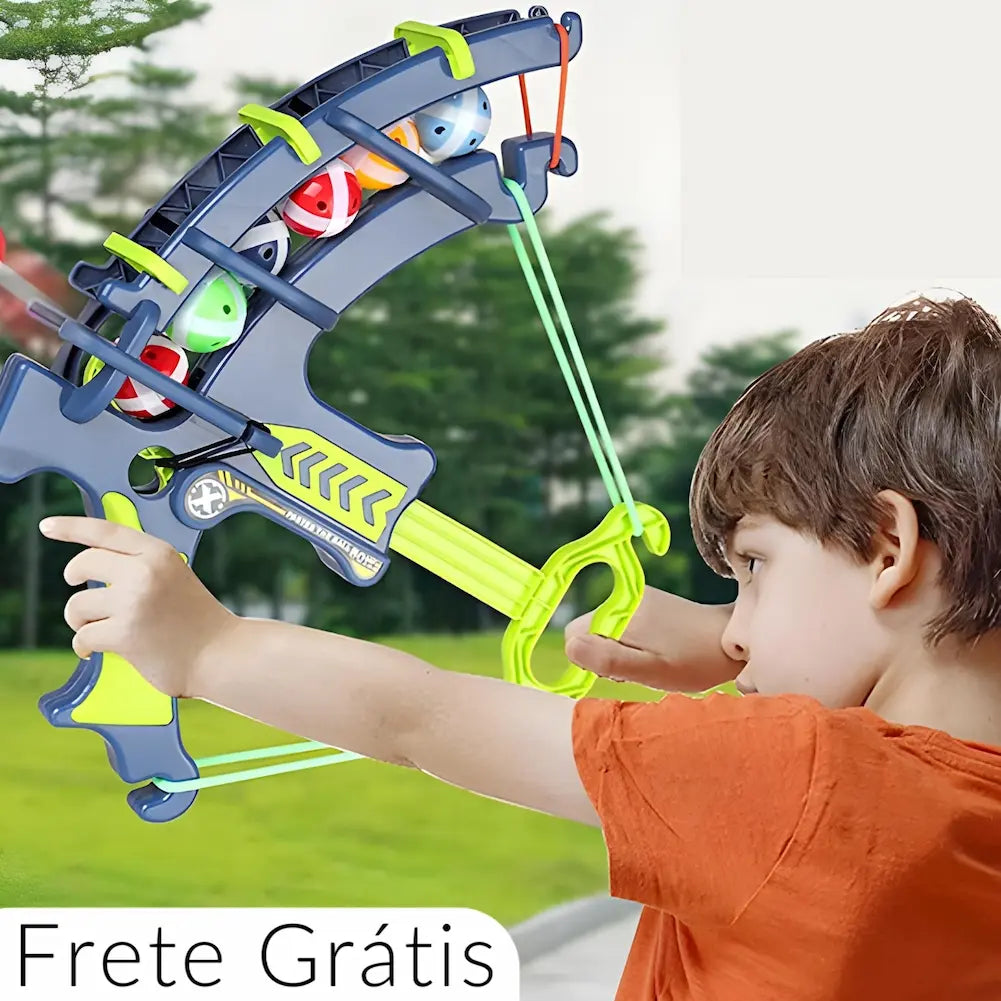 Imagem de uma criança brincando ao ar livre com um arco de brinquedo azul e verde. O arco está carregado com bolas coloridas (vermelha, azul, verde) e a criança está puxando a corda para lançar uma bola. O texto "Frete Grátis" está no canto inferior esquerdo da imagem.