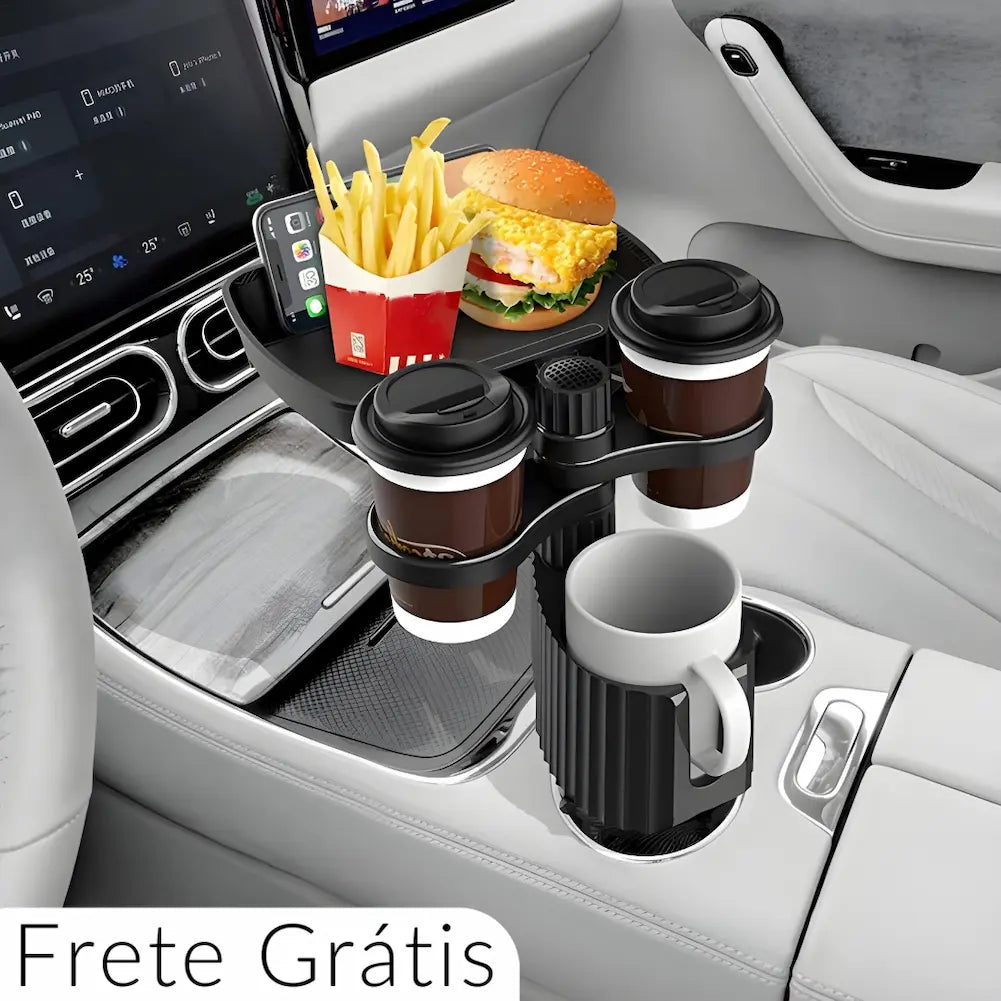 A imagem mostra um suporte giratório instalado no console central de um carro, contendo uma bandeja com um hambúrguer, batatas fritas e um celular. Abaixo, há suportes para três copos de café e uma caneca. O interior do carro é moderno, com acabamento em couro claro e tela digital no painel. Texto "Frete Grátis" está visível na parte inferior.