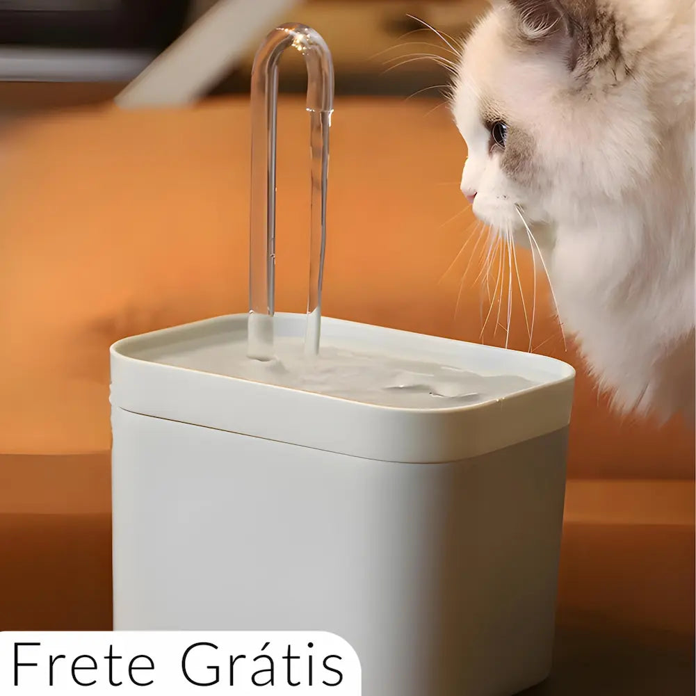  Imagem de um bebedouro para pets com um tubo curvado de onde sai água. Um gato branco com manchas cinza está próximo, olhando o fluxo de água. O bebedouro é branco e quadrado, com fundo desfocado em tons de laranja. Texto "Frete Grátis" aparece no canto inferior esquerdo.