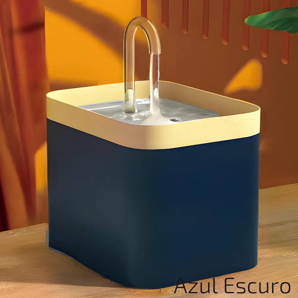 Imagem de um bebedouro quadrado para pets, com base azul escura e borda superior bege. A água flui suavemente de um tubo curvado no topo. O fundo é em tons de laranja e verde. Este é o modelo "Azul Escuro", ideal para quem busca um visual sofisticado.