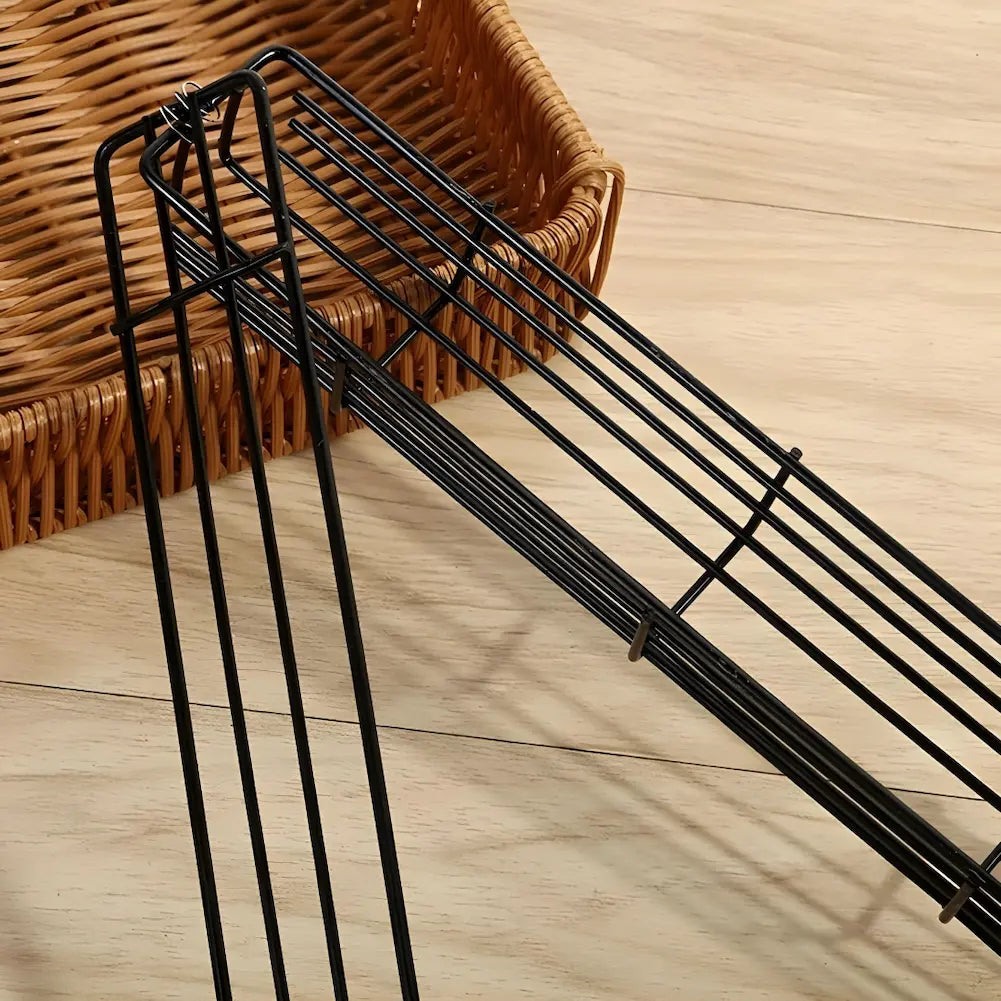 A imagem mostra uma cesta de vime em segundo plano e uma estrutura de metal em primeiro plano, que parece ser parte de um espeto de cesta para churrasco. A superfície é de madeira clara, e a estrutura metálica está vazia, destacando suas barras de metal paralelas e organizadas.