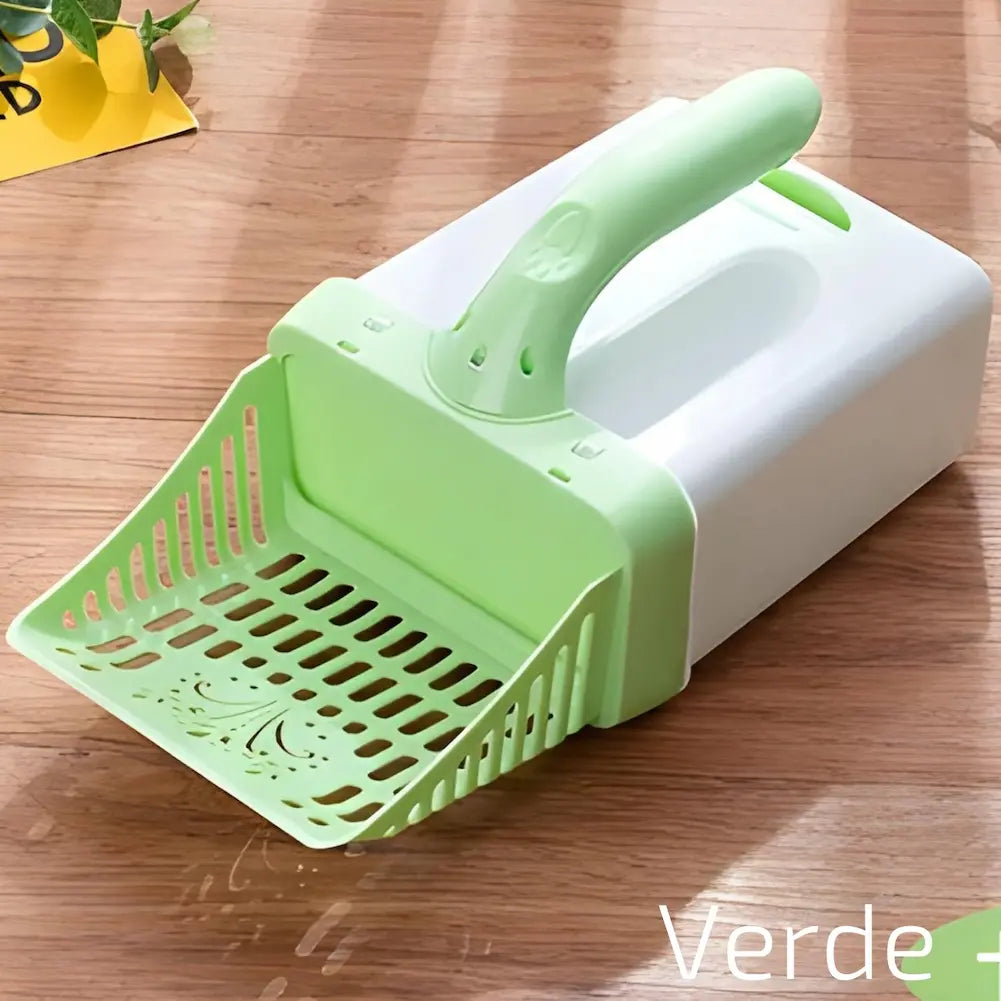 Imagem mostra uma pá de limpeza verde para caixa de areia de gato, acoplada a um cesto branco. A pá tem detalhes vazados e está sobre uma superfície de madeira. No canto inferior direito, há a palavra "Verde" escrita em texto branco. Há um vaso de planta no canto superior esquerdo.