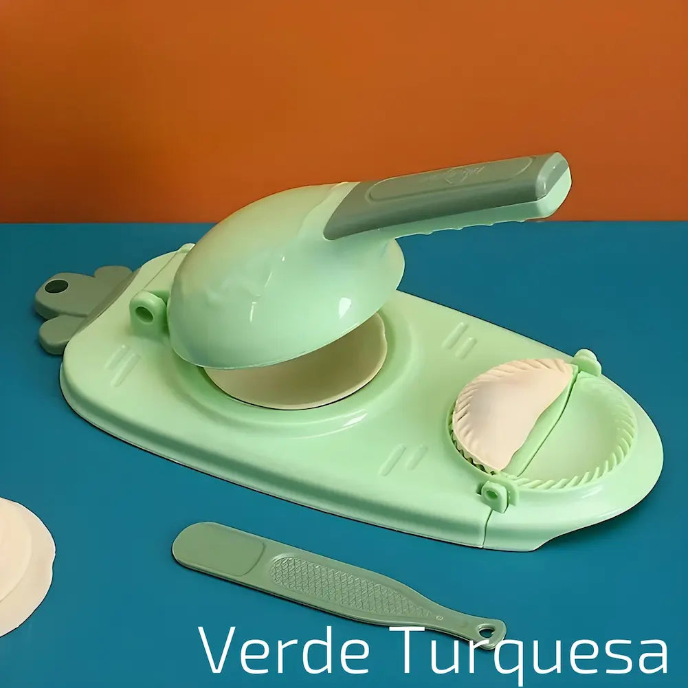  A imagem mostra um modelador manual de dumplings verde turquesa sobre uma superfície azul e uma parede laranja. O aparelho está aberto com um disco de massa no centro e um dumpling moldado ao lado. Há uma espátula verde e um disco de massa adicional ao lado. O texto "Verde Turquesa" está na parte inferior direita.