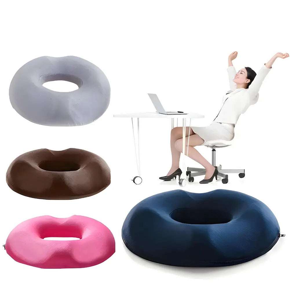 Imagem mostra uma mulher relaxando em uma cadeira de escritório, esticando os braços. Ela está usando uma almofada donut. À esquerda, três almofadas donut: uma cinza, uma marrom e uma rosa. Em primeiro plano, uma grande almofada azul. Uma mesa branca com laptop está ao fundo. Fundo branco.