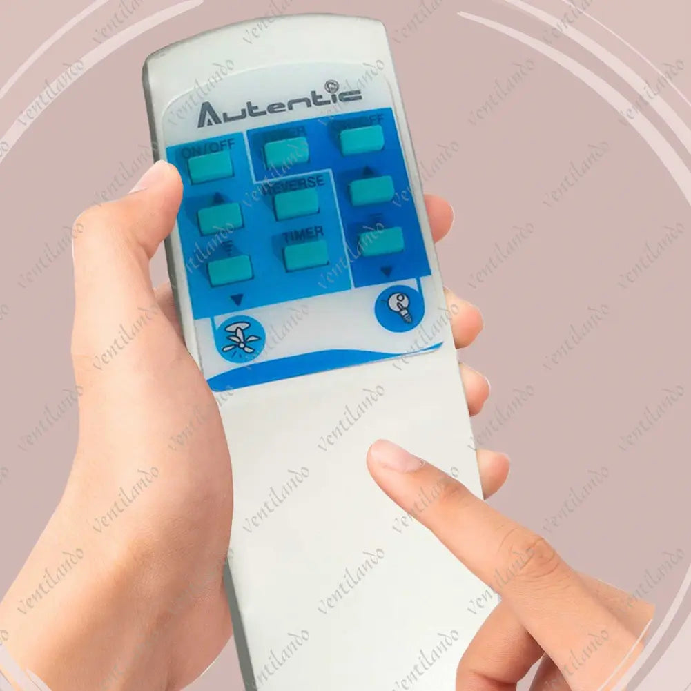 A imagem mostra um controle remoto para ventilador de teto da marca "Autentic". O controle é segurado por uma mão e possui botões azuis rotulados como ON/OFF, TIMER, REVERSE, e outros. O fundo é rosa claro com padrões circulares.