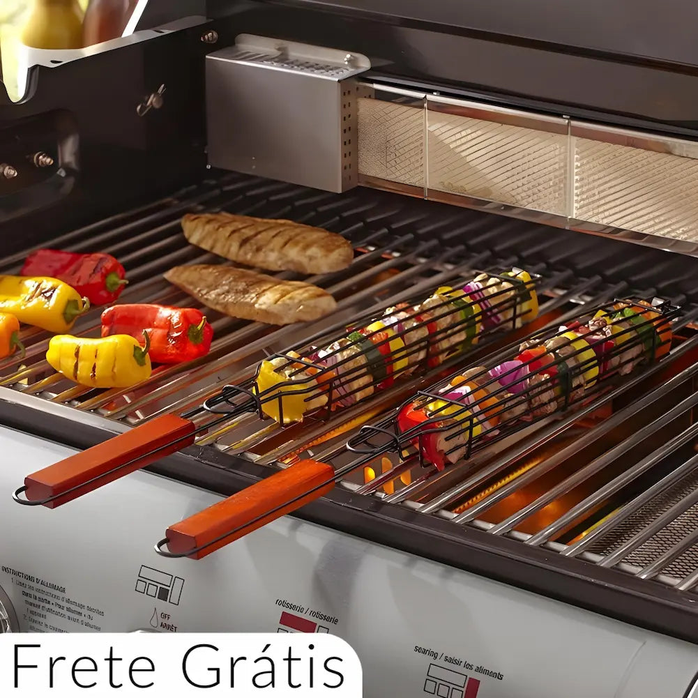 A imagem mostra uma grelha de churrasco com espetos de cesta contendo legumes variados, como pimentões e cogumelos, e pedaços de carne grelhando. Os espetos têm alças de madeira e a frase "Frete Grátis" está visível na parte inferior da imagem. Há também pedaços de pimentões e filés de frango diretamente na grelha.