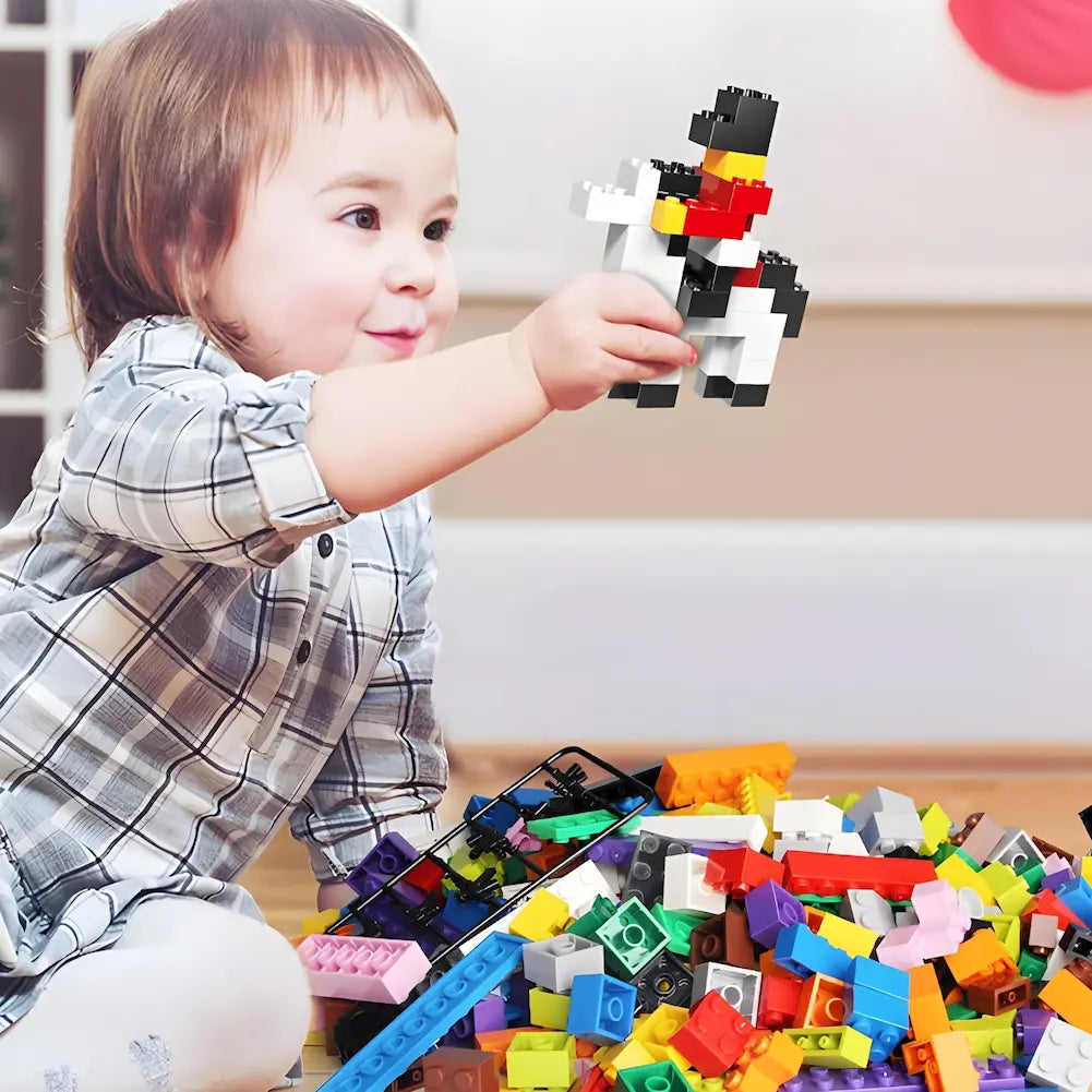 A imagem mostra uma criança pequena sorrindo enquanto brinca com blocos de montar coloridos. A criança segura uma construção feita com os blocos, enquanto uma grande pilha de peças está à sua frente. A cena sugere um momento de diversão e criatividade com brinquedos educativos.