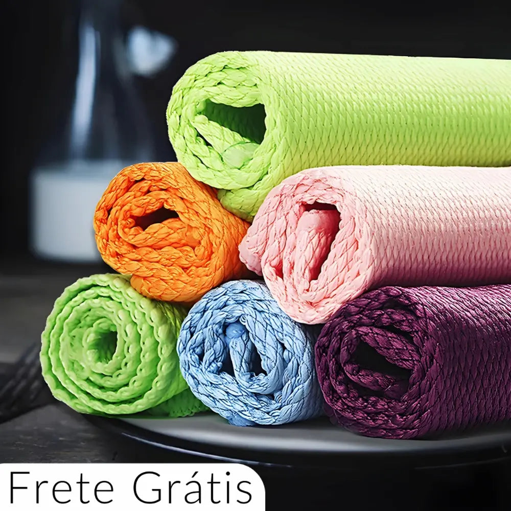  Seis panos de microfibra coloridos estão enrolados e empilhados. As cores são verde claro, laranja, rosa, azul claro, roxo e lilás. Na parte inferior esquerda, há um texto dizendo "Frete Grátis". Ao fundo, há um objeto desfocado.