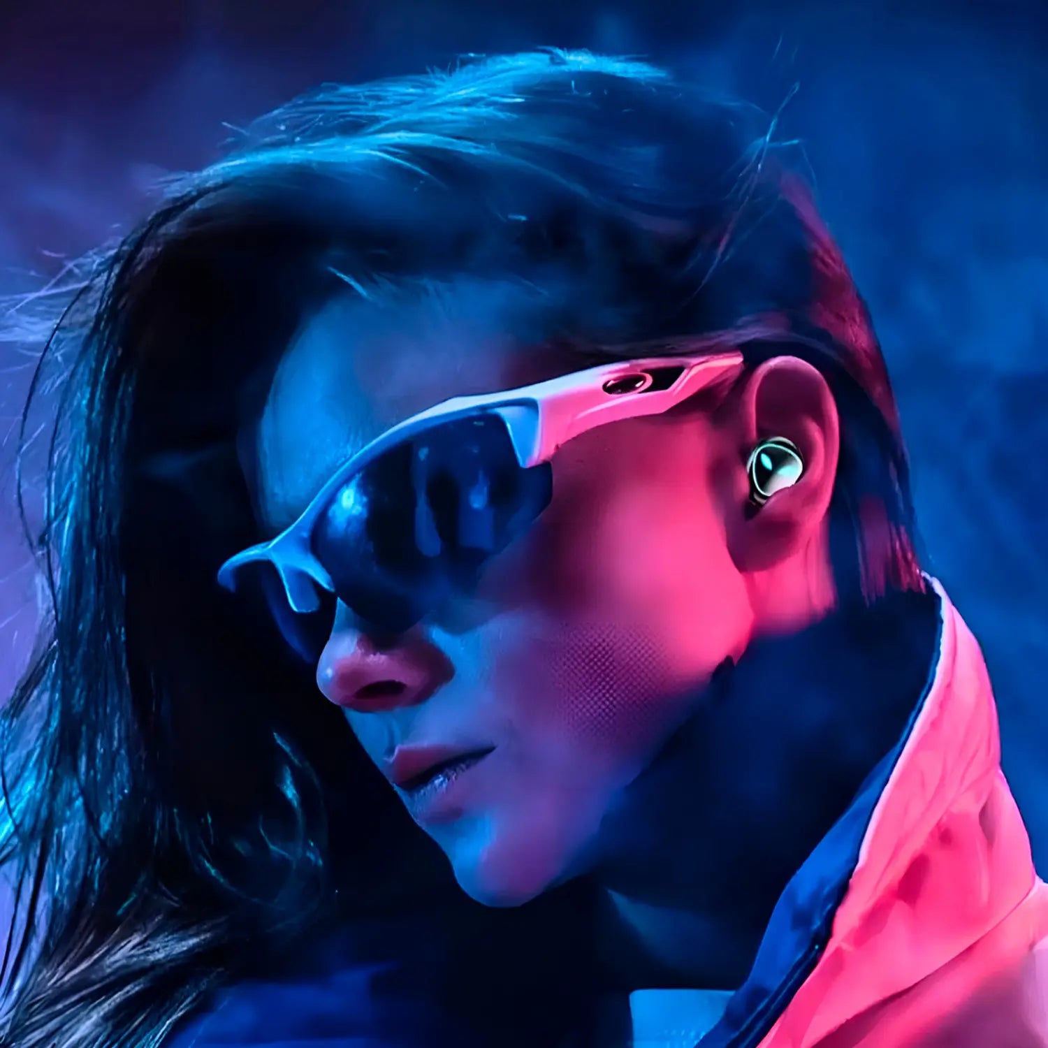 A imagem mostra uma mulher usando fones de ouvido sem fio e óculos escuros, com um estilo moderno e ousado. O fundo é iluminado com luzes vibrantes em tons de azul e rosa, criando uma atmosfera energética e futurista. A mulher tem uma expressão séria, e seu visual é completo com uma jaqueta estilosa. Os fones de ouvido são pequenos e discretos, realçando ainda mais o visual arrojado e contemporâneo do conjunto.