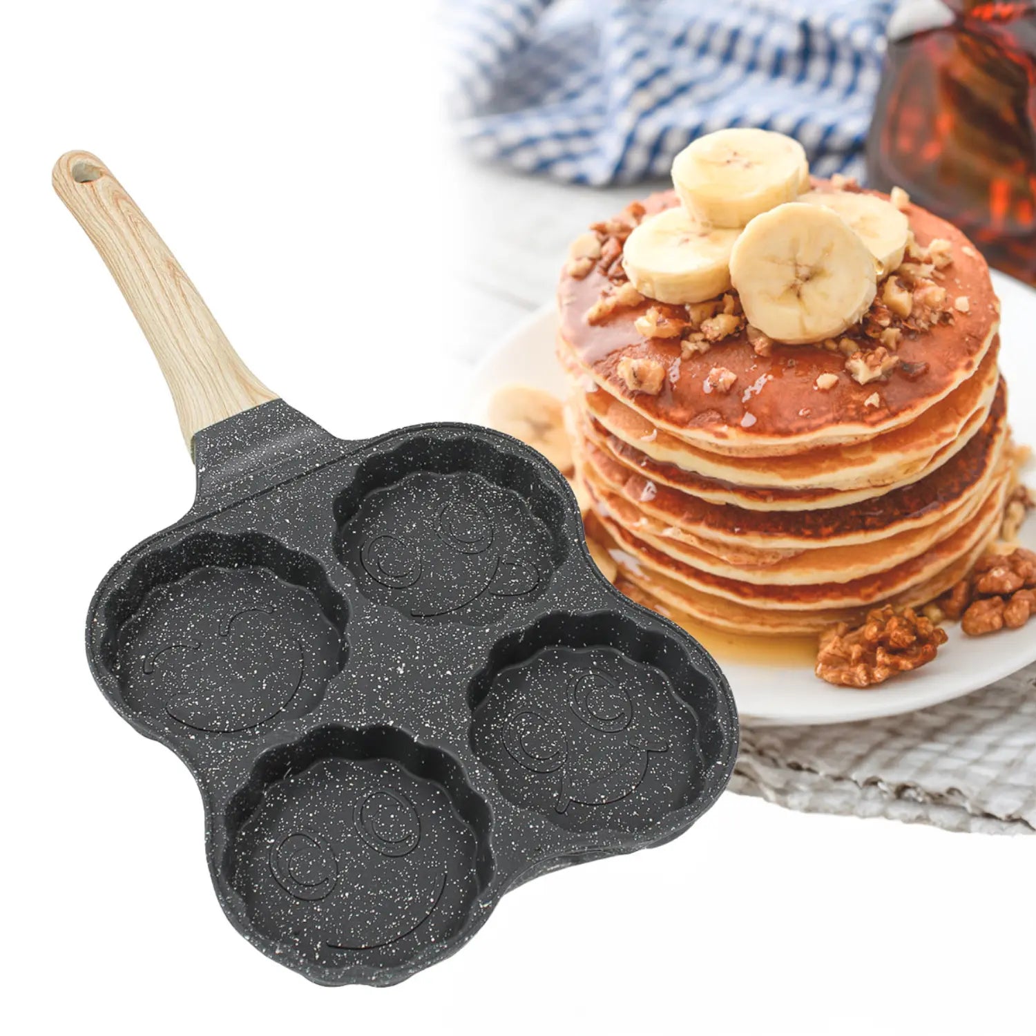 A imagem mostra uma frigideira com quatro cavidades circulares, cada uma com um design arredondado e uma superfície preta com manchas brancas, semelhante ao granito. A alça de madeira é visível na parte superior. Ao lado da frigideira, há uma pilha de panquecas cobertas com fatias de banana e nozes, criando uma composição apetitoso e acolhedora.