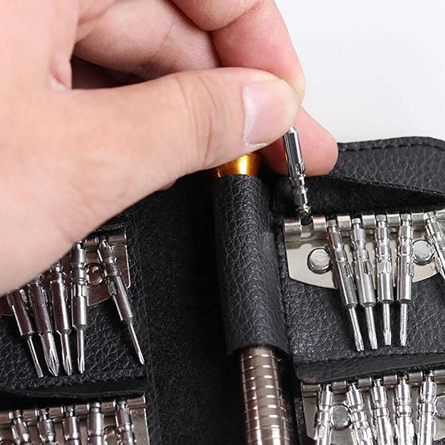 A imagem mostra um conjunto de ferramentas de precisão, com uma pessoa segurando um pequeno bit que está sendo inserido em uma chave de fenda ou ferramenta similar. O conjunto é organizado em uma capa, com vários bits de diferentes tamanhos e formatos, ideal para realizar reparos detalhados ou trabalhos de eletrônica e outras áreas que exigem precisão.