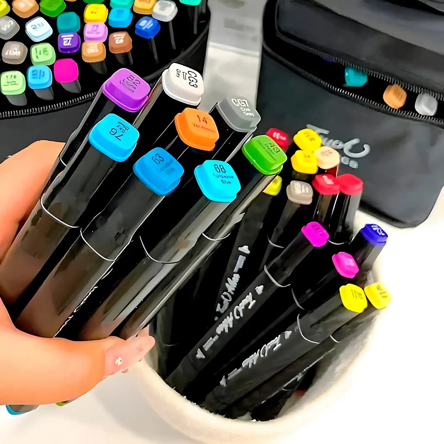 A imagem mostra uma mão segurando alguns marcadores coloridos, com tampas em tons de roxo, azul, amarelo e verde. Ao fundo, é possível ver mais marcadores organizados em um recipiente branco, com outras cores visíveis, como rosa e vermelho. A embalagem preta ao fundo contém mais marcadores, e o design moderno das tampas facilita a identificação das cores. O conjunto de marcadores é bem organizado e colorido, proporcionando uma visualização clara das diversas opções.