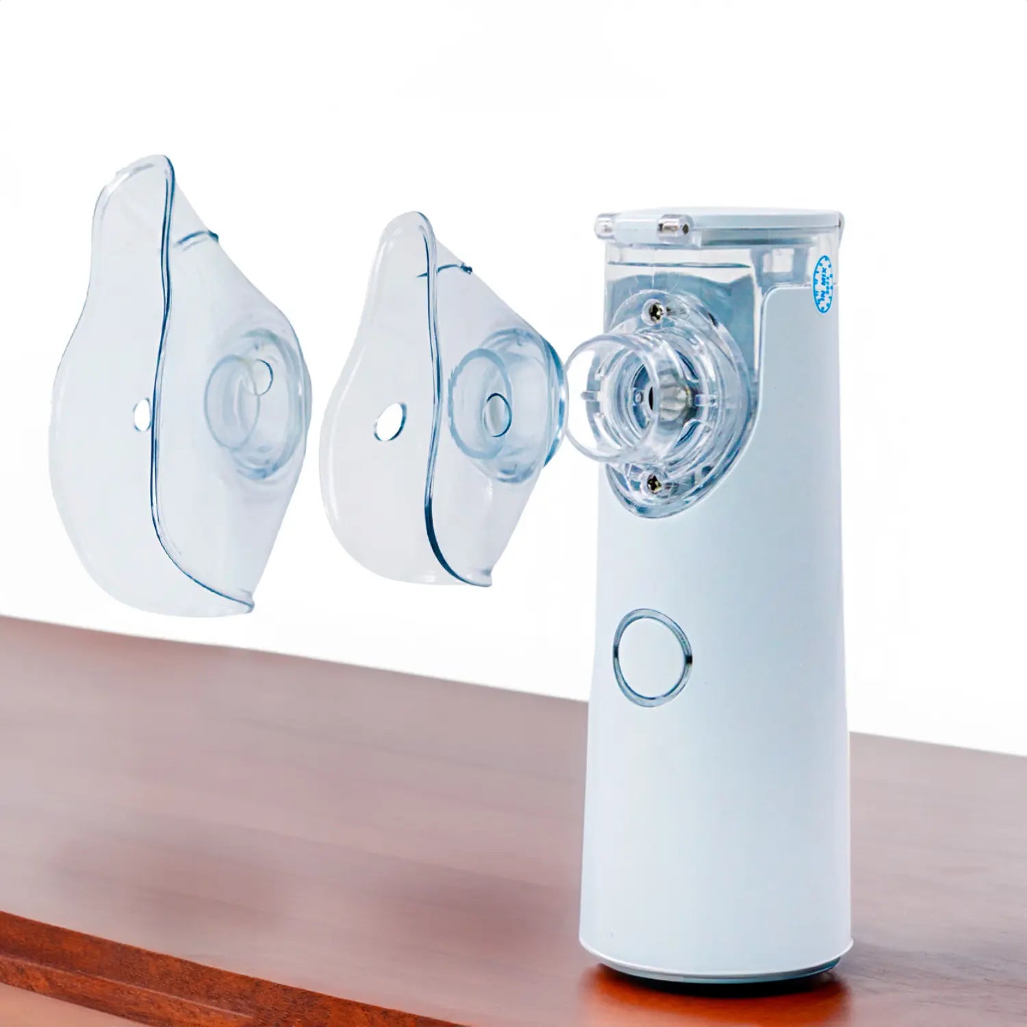 A imagem mostra um nebulizador branco com dois bocais transparentes ao lado. Um bocal parece ser para uso adulto e o outro para crianças, oferecendo versatilidade. O dispositivo é projetado para ser fácil de usar e adaptar conforme as necessidades do usuário, com uma estrutura simples e eficiente.