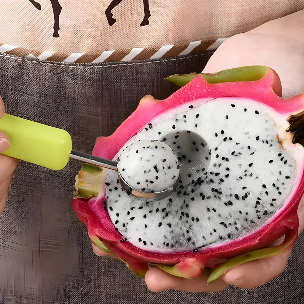  A imagem mostra uma mão segurando uma pitaya cortada ao meio. Outra mão usa uma colher arredondada com cabo verde para retirar uma bola da polpa branca com sementes pretas da fruta. A casca da pitaya é rosa vibrante e a polpa branca é pontilhada com pequenas sementes.