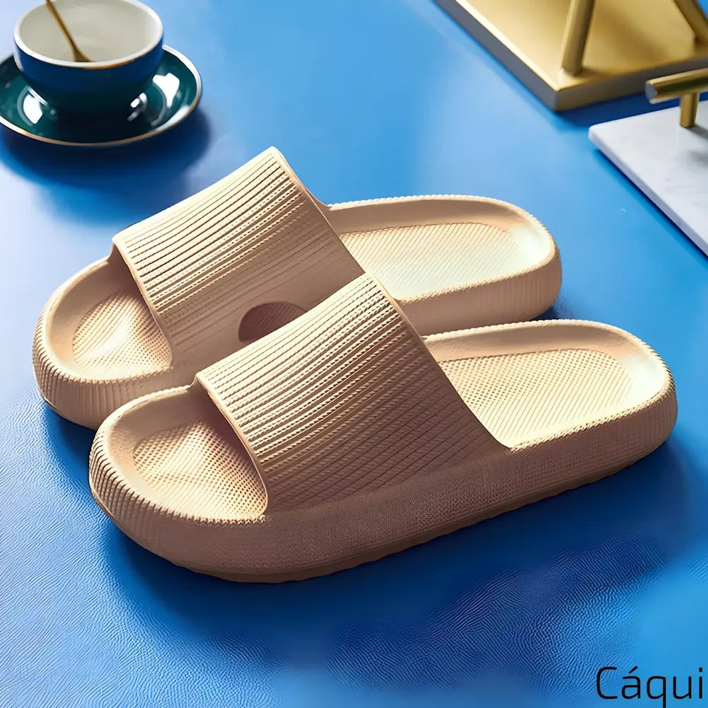 Imagem mostrando um par de chinelos cáqui. Eles estão dispostos sobre uma superfície azul, com um ambiente que inclui uma xícara de chá e um livro, destacando o conforto e o design prático.