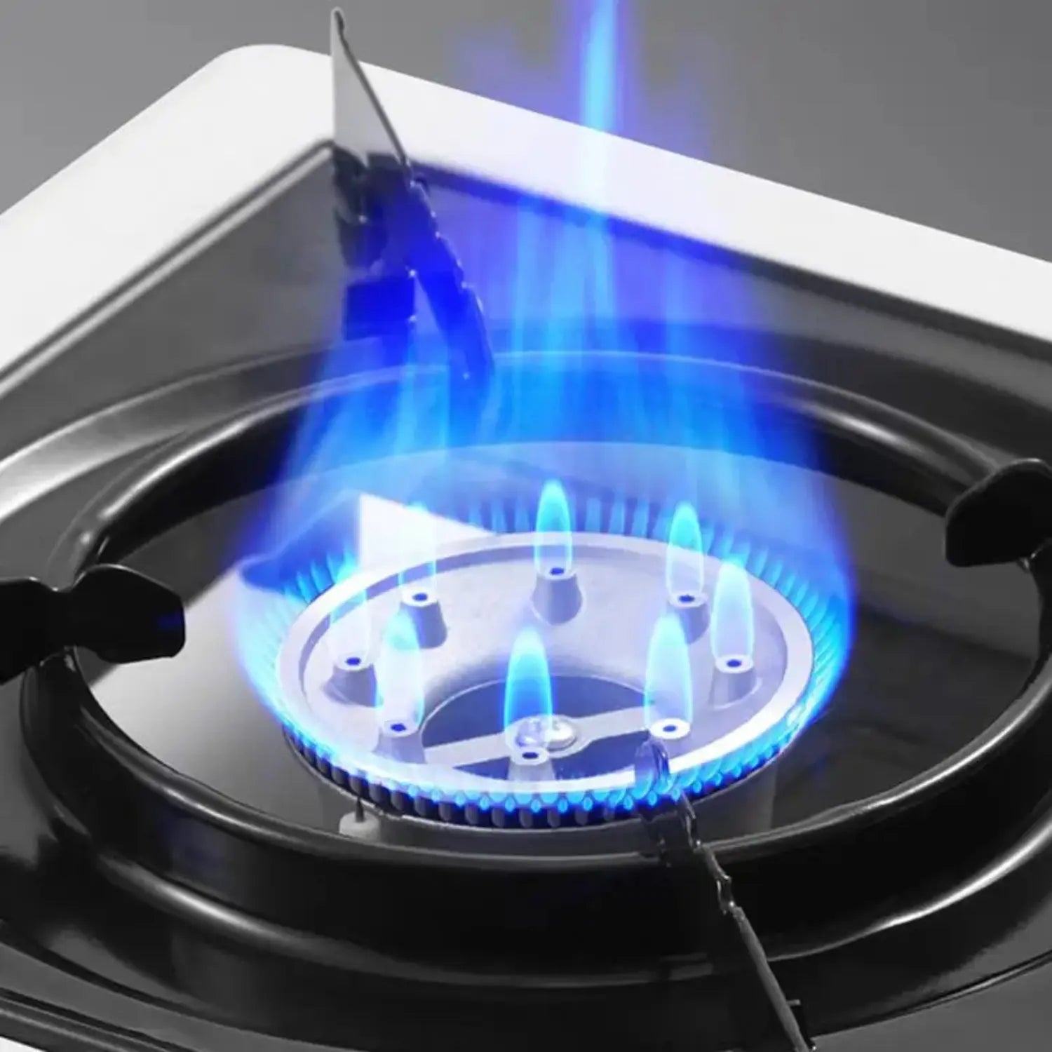 A imagem mostra o detalhe da chama azul de um queimador de fogão a gás, evidenciando a eficiência e a distribuição uniforme do fogo. A chama está visivelmente controlada e limpa, sugerindo um uso seguro e eficaz do gás. O design do queimador é simples, mas robusto, com a chama destacando-se como um ponto focal, mostrando a potência do equipamento.