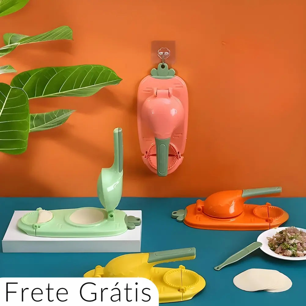 A imagem mostra quatro modeladores manuais de dumplings em cores diferentes (verde, laranja, amarelo e rosa) sobre uma superfície azul e pendurado em uma parede laranja. Há folhas de planta no lado esquerdo. Na frente, há discos de massa, uma espátula verde e um prato com recheio. O texto "Frete Grátis" está na parte inferior.