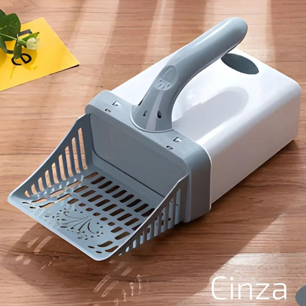  Imagem mostra uma pá de limpeza cinza para caixa de areia de gato, acoplada a um cesto branco. A pá tem detalhes vazados e está sobre uma superfície de madeira. No canto inferior direito, há a palavra "Cinza" escrita em texto branco. Há um vaso de planta no canto superior esquerdo.