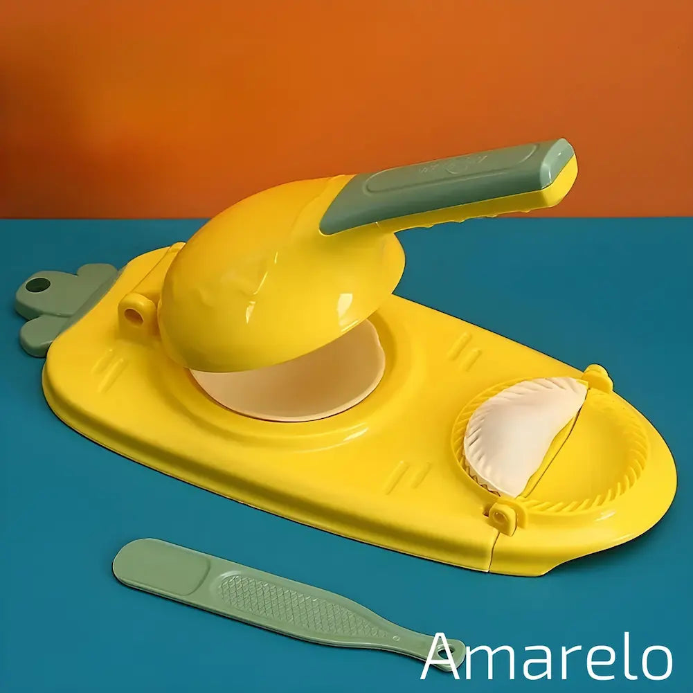  A imagem mostra um modelador manual de dumplings amarelo sobre uma superfície azul e uma parede laranja. O aparelho está aberto com um disco de massa no centro e um dumpling moldado ao lado. Há uma espátula verde e um disco de massa adicional ao lado. O texto "Amarelo" está na parte inferior direita.