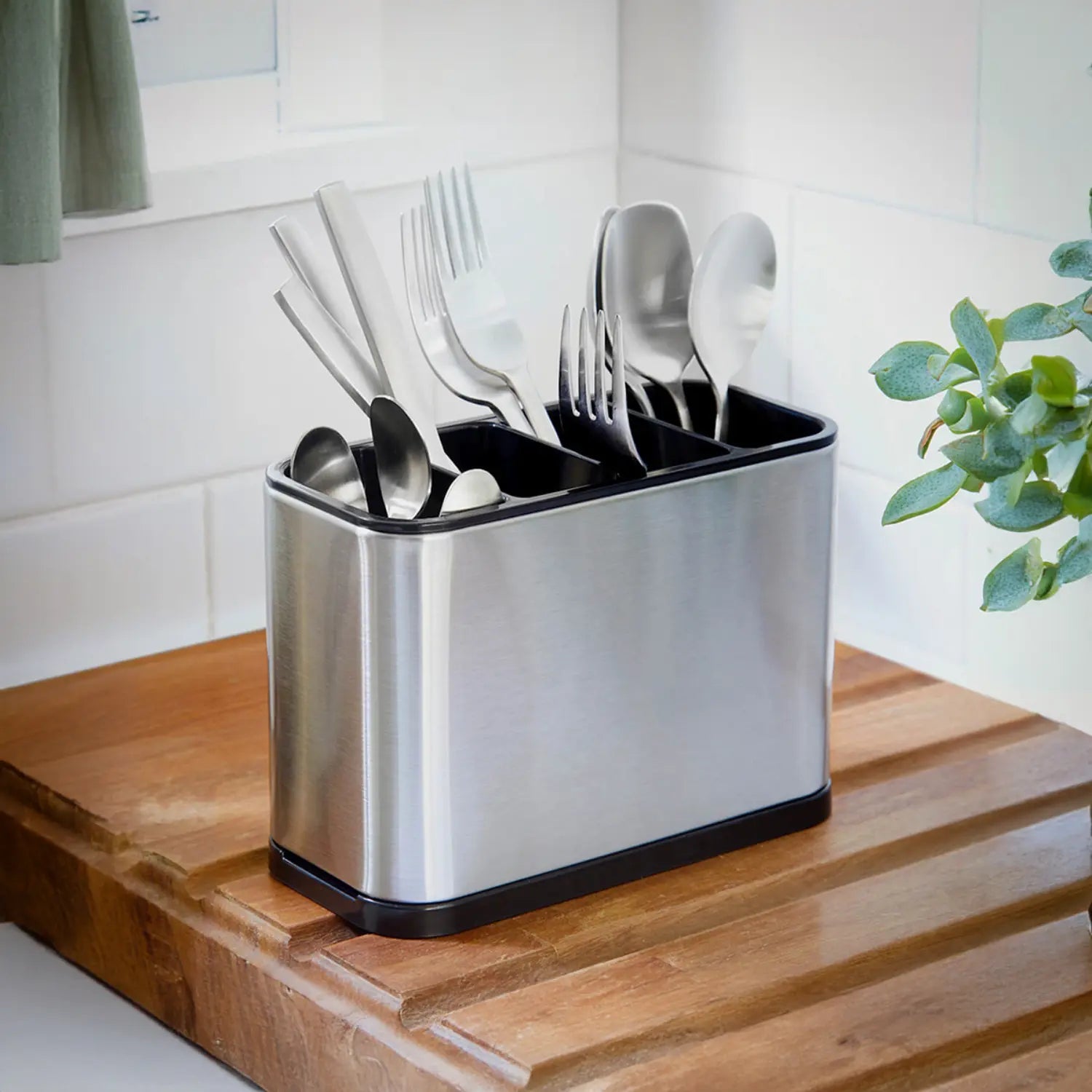 A imagem mostra o porta-talheres de aço inoxidável, agora com talheres organizados no interior. Facas, garfos, colheres e outros utensílios estão bem dispostos, proporcionando uma maneira prática e organizada de manter os talheres na cozinha. O design é elegante, combinando com qualquer estilo de cozinha, e a base preta oferece estabilidade e praticidade