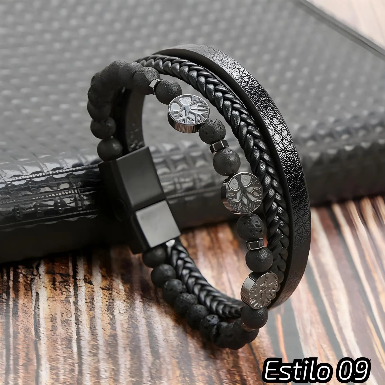 Pulseira preta com couro trançado, tiras texturizadas e contas escuras. Adornada com três medalhões metálicos com símbolos variados. Fecho preto, ideal para um estilo elegante e minimalista. Estilo: 09.