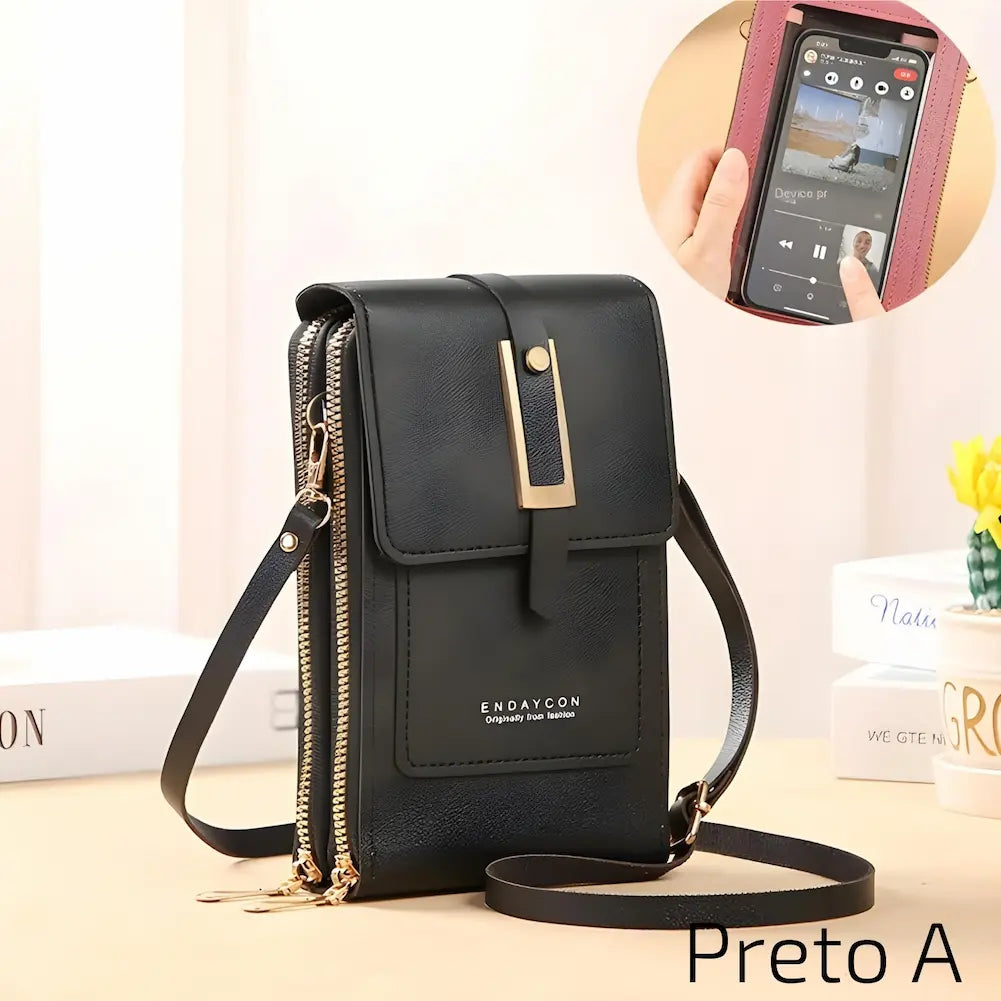 Bolsa de couro preto com alça ajustável e fecho metálico dourado. Tem dois zíperes laterais e um bolso frontal com o nome "ENDAYCON". No canto inferior direito, o código "Preto A", uma das opções de compra.