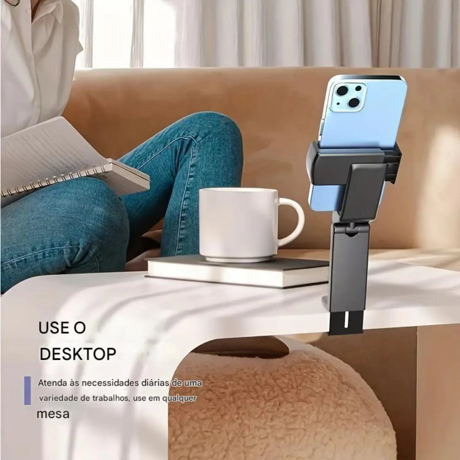 A imagem mostra um suporte de mesa para celular. O suporte está preso à borda de uma mesa, com um smartphone apoiado nele. A pessoa na imagem está sentada, ao lado de uma xícara de café, com um livro aberto na mesa. A legenda abaixo da imagem sugere que o suporte é útil para atividades diárias, especialmente para trabalhos ou uso ao ar livre.