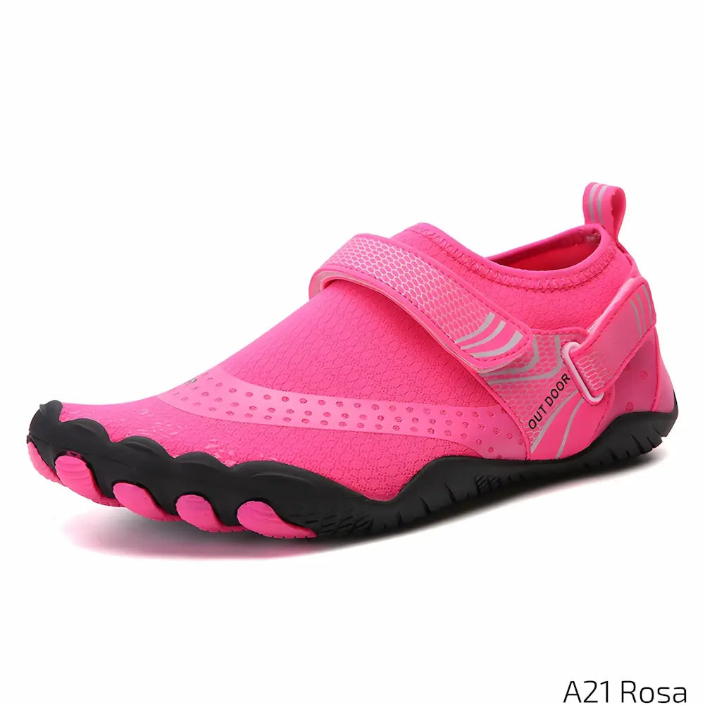 A imagem mostra um tênis esportivo de cor rosa com detalhes em preto e cinza. O modelo possui uma faixa de velcro na parte superior, substituindo os cadarços. A sola é preta com detalhes texturizados para maior aderência. Na parte traseira, há uma alça. No canto inferior direito, está escrito "A21 Rosa".