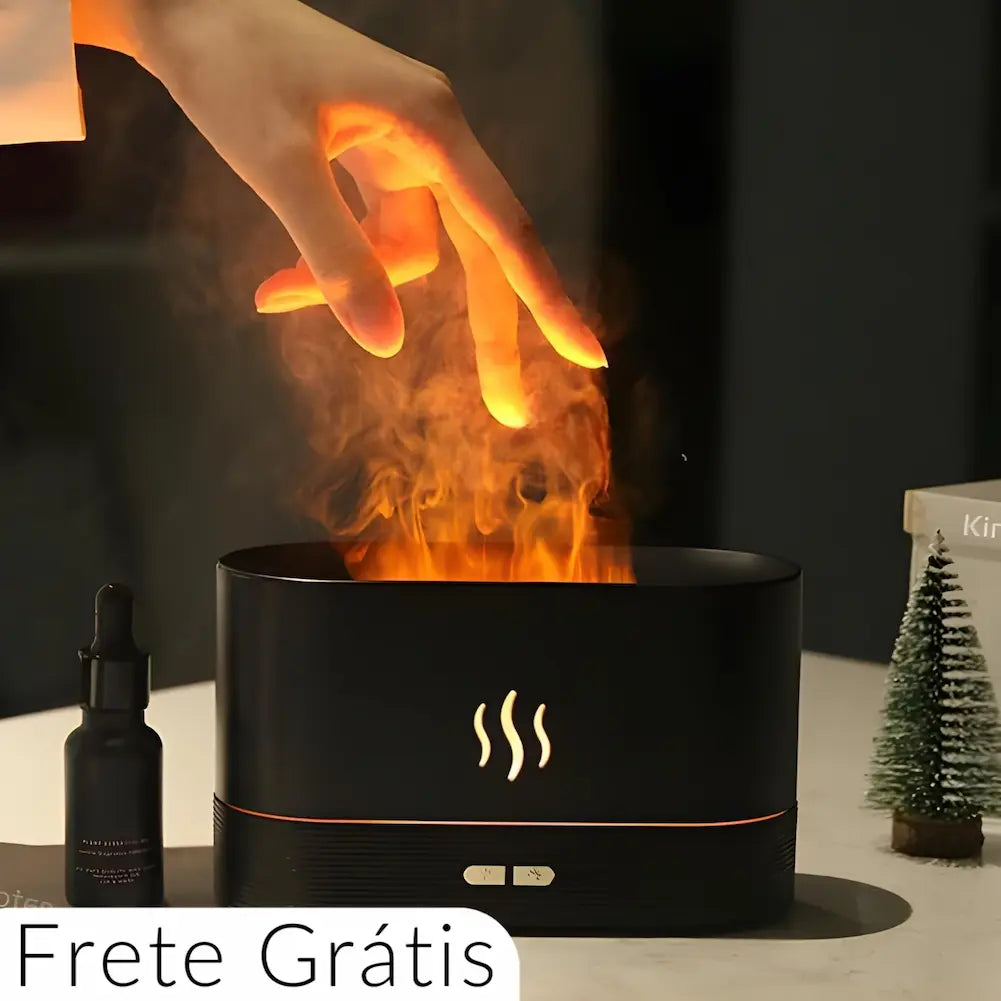 Imagem de um umidificador de ar preto emitindo vapor iluminado em laranja, criando um efeito de chama. Uma mão está suspensa acima do vapor, tocando-o suavemente. Ao lado do umidificador, há um frasco de óleo essencial. O texto "Frete Grátis" está na parte inferior esquerda da imagem.