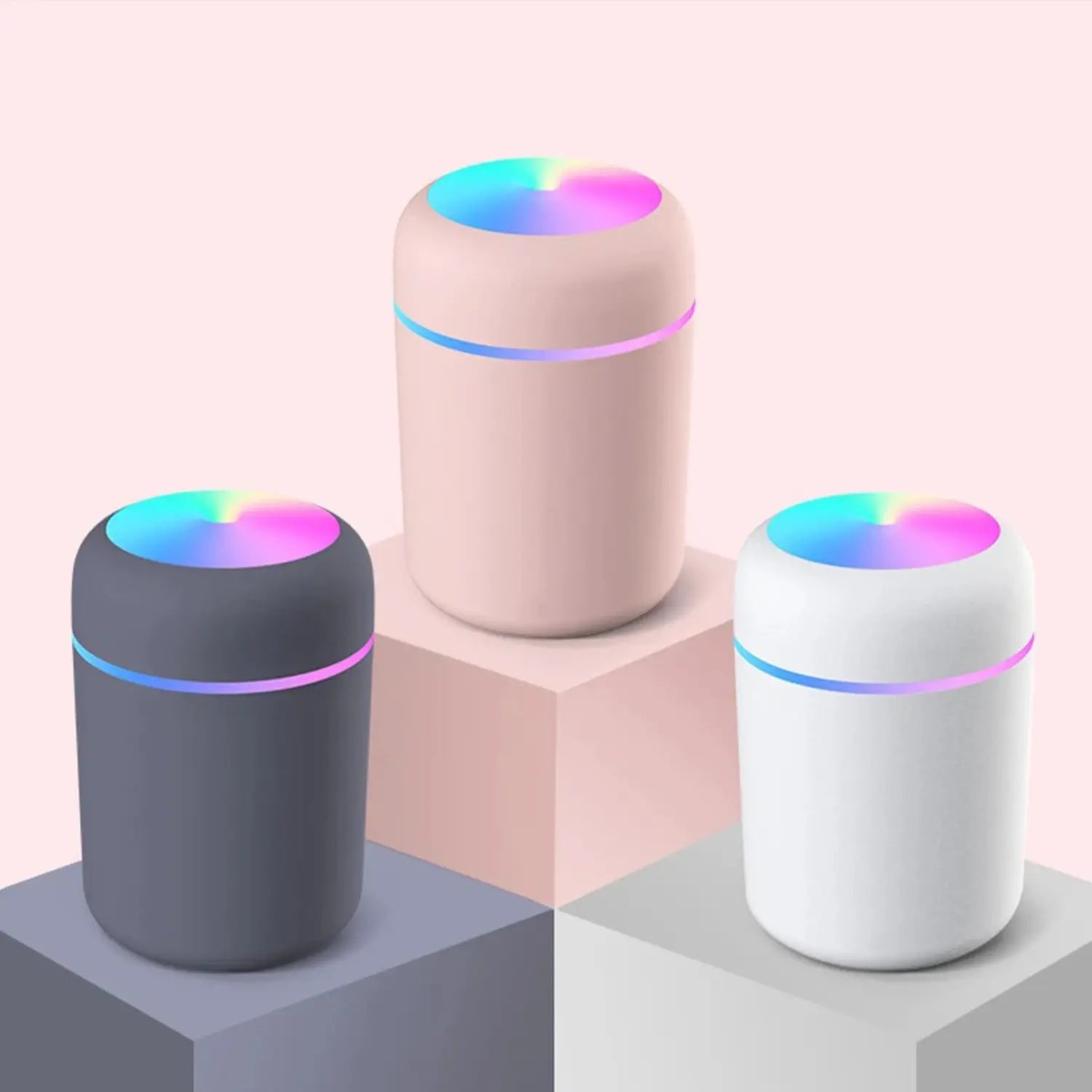 A imagem exibe três umidificadores de ar em cores distintas: cinza, rosa e branco, todos com detalhes de luz LED colorida na parte superior, criando um efeito visual atrativo. O design simples e moderno proporciona uma atmosfera relaxante, enquanto o formato compacto é ideal para qualquer ambiente, oferecendo tanto funcionalidade quanto estilo.