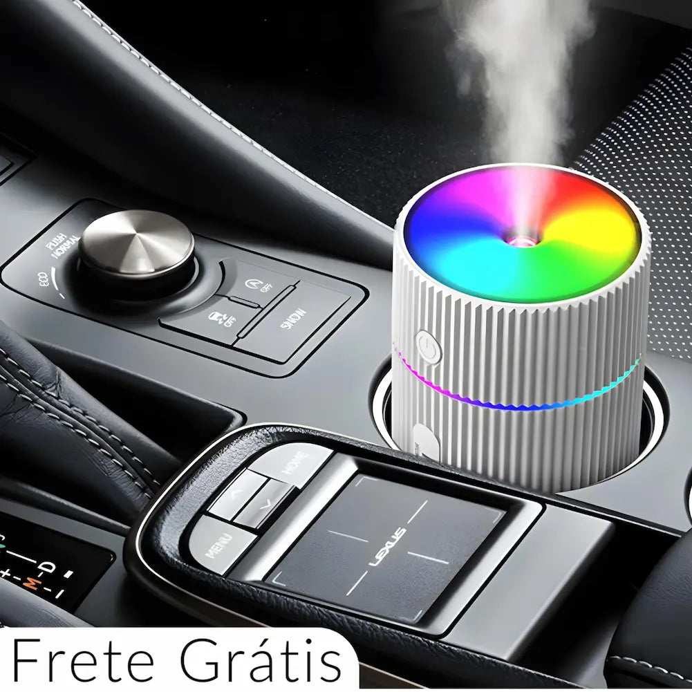 Imagem de um umidificador de ar portátil branco, com textura ondulada, colocado no porta-copos de um carro. O topo do umidificador emite luzes coloridas em arco-íris, e há um anel luminoso ao redor do meio do aparelho. O console do carro possui botões e controles prateados e pretos, e a imagem inclui o texto "Frete Grátis" na parte inferior.