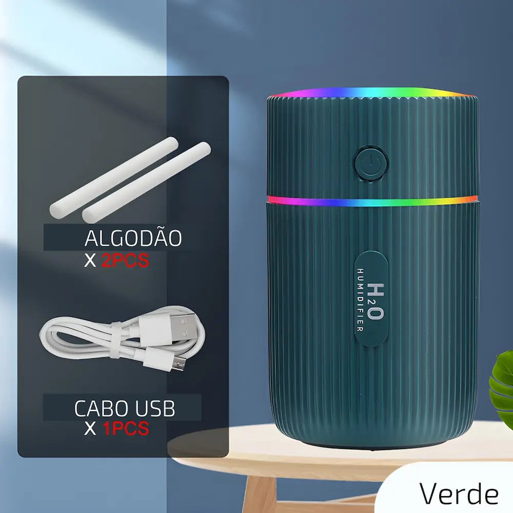 Imagem mostrando um umidificador de ar portátil verde com textura ondulada, emitindo luzes coloridas no topo. Ao lado, há uma representação dos acessórios incluídos: duas peças de algodão cilíndricas e um cabo USB branco. Abaixo dos acessórios, há textos indicando "ALGODÃO X 2PCS" e "CABO USB X 1PCS". Na parte inferior da imagem, lê-se "Verde".